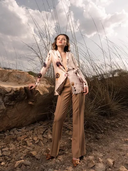 A wide shot that places the model and her outfit within the expansive landscape. The dramatic sky and earthy tones complement the printed blazer and flared trousers, creating a high-impact campaign image.