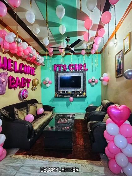 A wide shot of the living room decorated in pink and white for a baby girl's arrival. The balloons on the ceiling and the arrangements around the furniture create an immersive and joyful environment.