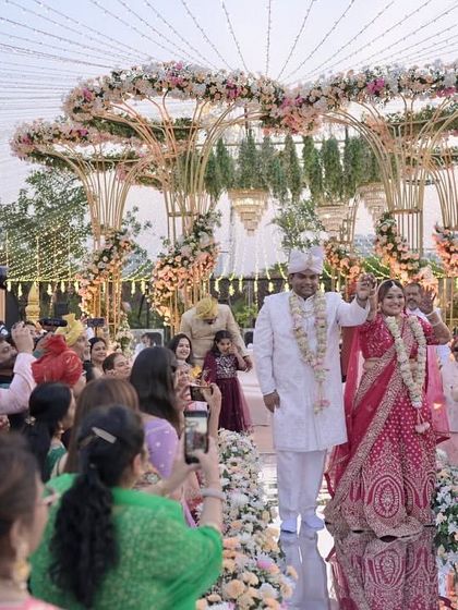 The couple's grand entrance down the mirrored aisle, surrounded by guests, with the stunning floral mandap as their destination.