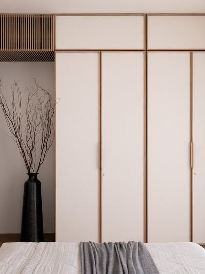 This view of the master bedroom showcases the custom white wardrobes with wood trim. The design maintains a clean, uncluttered look while providing ample storage, contributing to the room's serene atmosphere.