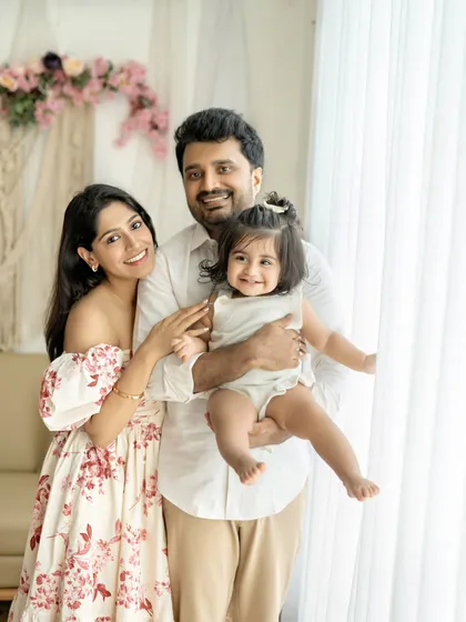 A beautiful family of three, posing by the window with their adorable daughter.