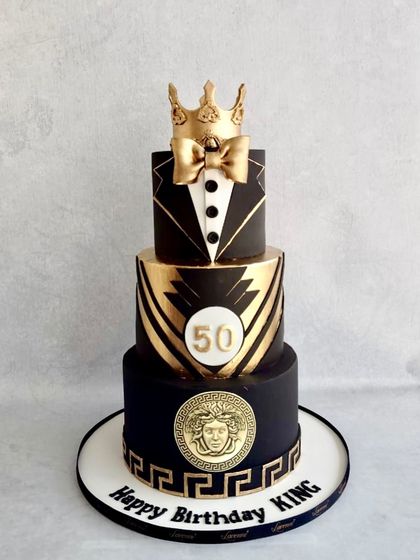 A cake fit for a king's 50th birthday. This three-tiered design in black and gold features a tuxedo on the top tier, a Versace-inspired Medusa plaque, and a golden crown.