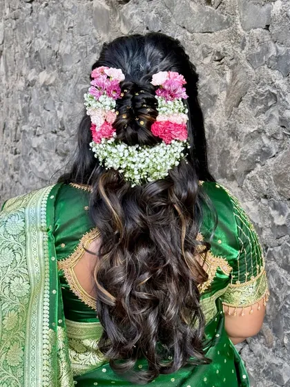 A hairstyle that is a work of art. This intricate half-up style features a braid woven with fresh baby's breath and carnations, perfect for a traditional yet fresh bridal look.