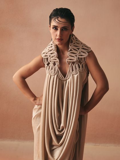 A powerful stance in the Kashar tunic. The corded statement collar and fluid cowl-drape create a silhouette that is both architectural and soft.