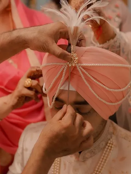 A close-up of the Sehra Bandi ritual, where the groom's turban is lovingly adorned by his family members before the ceremony begins.