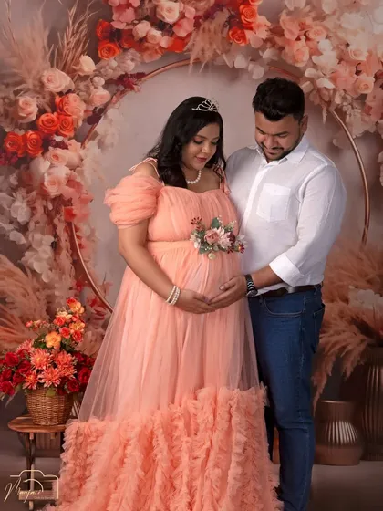 A serene and loving portrait of the couple, both gently holding the baby bump. The floral ring creates a magical, romantic backdrop.