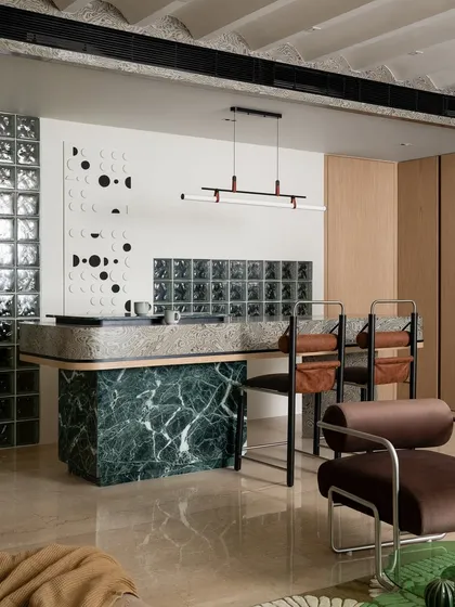 Details make the design. This multifunctional breakfast counter in the 'ARAH' home features a striking green marble base and a textured veneer top. The glass block wall behind it is not just a design element; it's a functional solution that allows soft, diffused light into the kitchen.