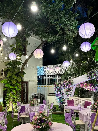 An enchanted evening garden party. The combination of hanging lanterns, string lights, and a purple-themed floral arch created a truly magical atmosphere for this celebration.