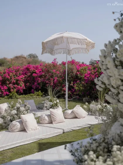 Low floor seating with plush white cushions and fringed umbrellas offers a traditional yet comfortable option for guests at the Anand Karaj.