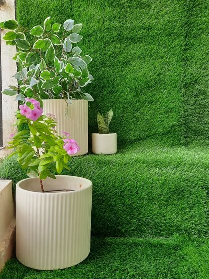 A close-up of the tiered seating I created using an artificial grass carpet. This setup not only provides a unique seating solution but also enhances the all-green, natural look of the balcony. The simple ceramic planters add a modern touch.