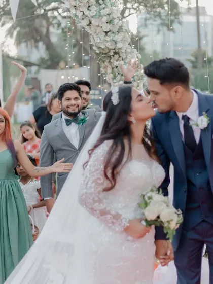 A beautiful kiss seals the vows at a Christian wedding, with the wedding party cheering in the background. I love capturing the energy and support of friends and family on the big day.