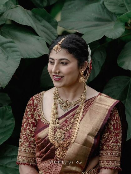 A bride in a stunning maroon and gold Kanchipuram silk saree. The blouse is fully embroidered with intricate patterns, creating a look of pure opulence.