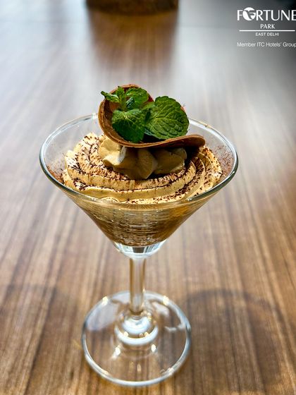 A deconstructed tiramisu or coffee-flavored mousse served in a martini glass, garnished with mint and a chocolate wafer.