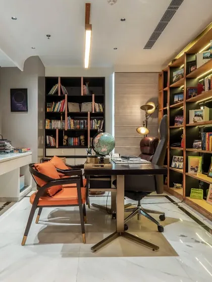 This home office was designed for focus and inspiration. It features floor-to-ceiling bespoke shelving with integrated backlighting to display books and artifacts, combining practical storage with a warm, sophisticated ambiance for a productive work environment.