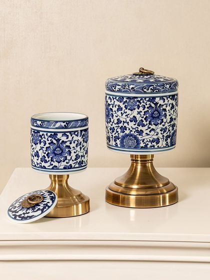 This set of two blue pottery jars showcases classic floral motifs on a modern cylindrical shape. The combination of handcrafted ceramic and a sturdy brass base makes them versatile for serving or as decorative accents.