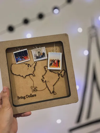 A perfect farewell gift for a friend moving from India to the USA. This custom map frame features laser-cut outlines of both countries, mini polaroids of shared memories, and a fun "Bring Dollars" message.