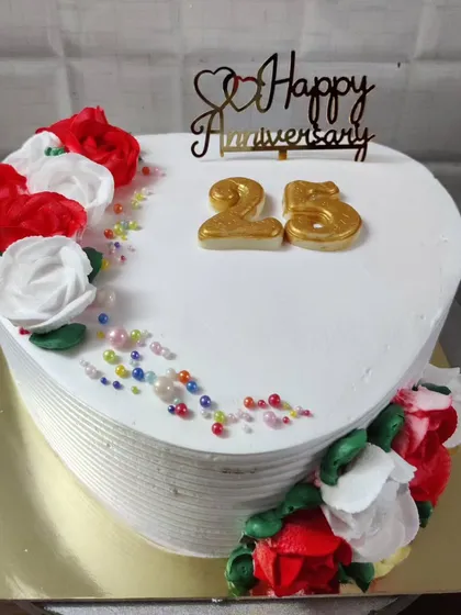 A heart-shaped cake for a 25th anniversary. It's decorated with red and white buttercream roses and colorful sprinkles for a festive look.