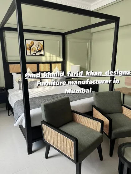 A complete hotel room setup featuring a modern black four-poster canopy bed with a cane headboard. The room is furnished with matching dark-finish accent chairs and a side table, showcasing a cohesive design language for contemporary hospitality projects.