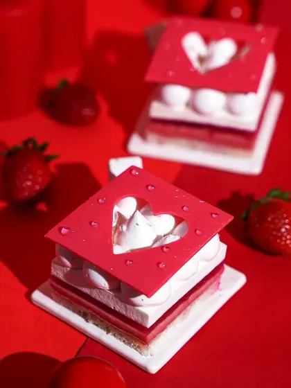 Delicate square-shaped Valentine's pastries with heart cutouts, styled on a solid red background. The clean, minimalist composition with dramatic lighting highlights the dessert's intricate design.