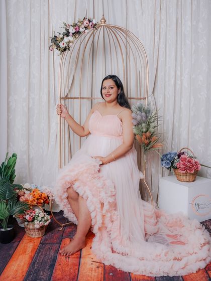 A lovely seated portrait in the golden birdcage, surrounded by flowers. The soft pink gown and whimsical props create a fairytale-like scene.