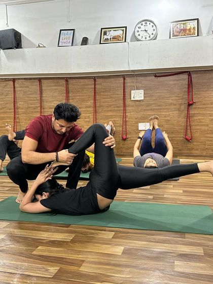 An instructor assists a student in a supine leg stretch, focusing on alignment and deepening the posture safely.
