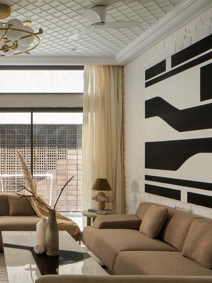 A bold, abstract black-and-white artwork hangs on a whitewashed brick wall, creating a striking focal point in the living room. The design balances raw textures with curated art.