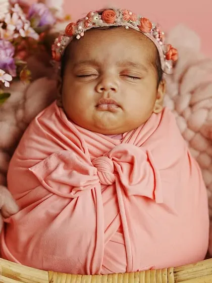The pure innocence of a sleeping newborn. This studio portrait features a baby girl swaddled in soft pink fabric, nestled in a basket adorned with a beautiful floral arrangement. We focus on creating a safe and serene environment for these delicate shots.