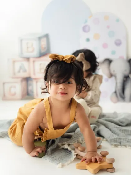 One twin crawls towards the camera while her sister sits in the background. A fun, dynamic shot from a twin toddler session.