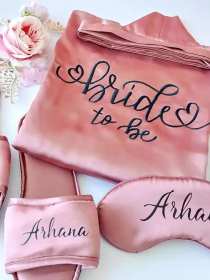 A "Bride to be" essentials kit, featuring a personalized satin robe, eye mask, and slippers. Perfect for getting ready on the big day.