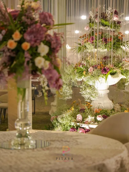 The floral fountain seen from a dining table, showing how the decor elements work together to create a cohesive and elegant atmosphere. The mirrored tabletop reflects the beauty of the arrangements.