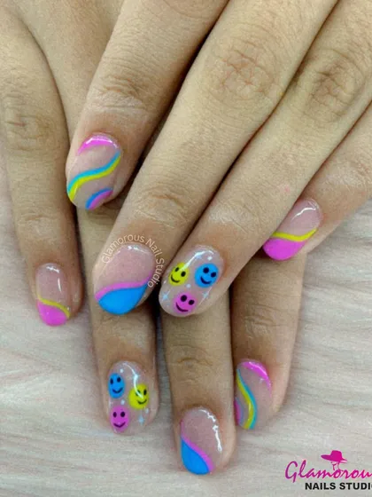 A cheerful and colorful design featuring multi-colored smiley faces on some nails, paired with abstract waves in pink, blue, and yellow on others.