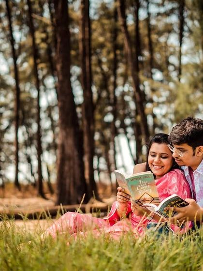 A sweet moment of the couple reading a book together, nestled in the grass in a beautiful woodland setting.