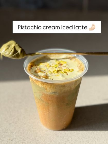 A beautiful shot of the Pistachio Cream Iced Latte, showcasing the creamy green topping and a spoonful of pistachio paste.