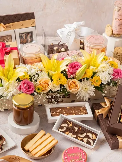 An abundant display of Diwali gifts, centered around a floral wooden crate hamper and surrounded by boxes of date squares, cookie jars, and tea cakes. This image illustrates the sheer variety and scale of my festive collection.