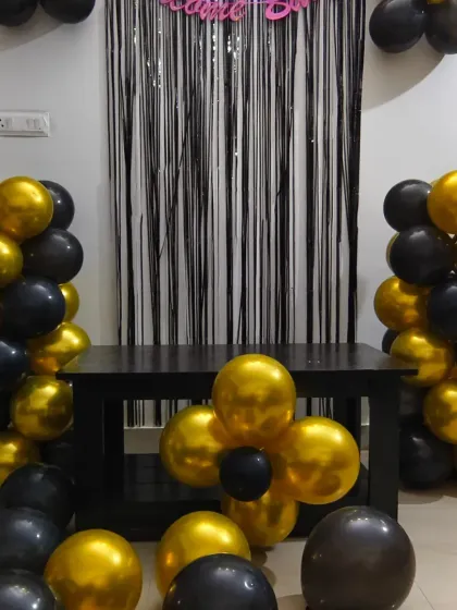 A bold and beautiful black and gold balloon decoration for a home party. This setup includes two balloon pillars and a flower-shaped balloon centerpiece, offering great value.