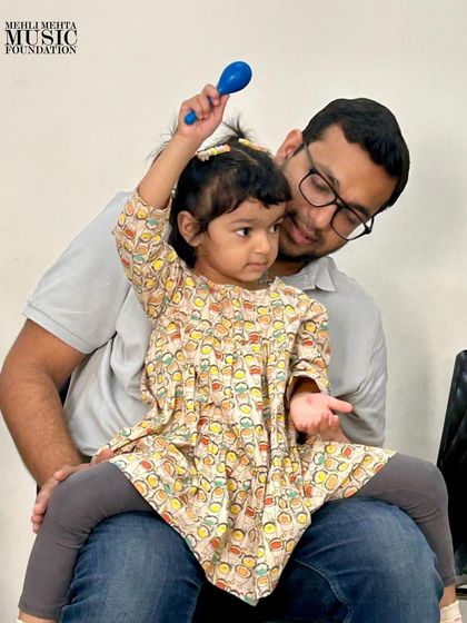 A father and daughter share a moment of musical discovery with a shaker. Our parent-toddler classes are designed to strengthen family bonds through shared creative activities.