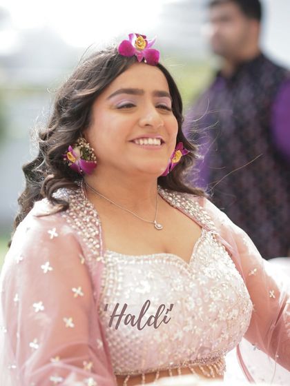 The pure joy of a Haldi ceremony captured in a smile. The makeup is light and fresh, with a hint of lilac on the eyes to match her floral jewellery.