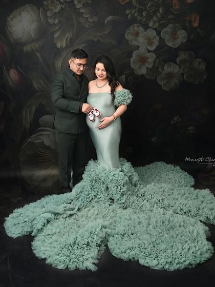 A sweet detail shot. The couple holds up a pair of tiny baby shoes over the bump, symbolizing their excitement for the new arrival.