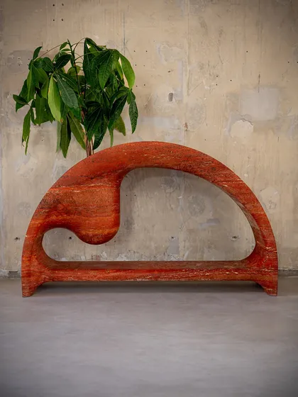 The Samaveta Console in red travertine, shown here with a plant to highlight its organic, sculptural form. The piece is designed to be a harmonious blend of raw material power and elegant, fluid lines.