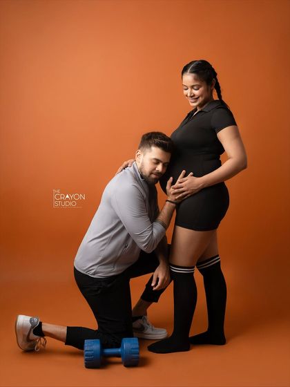 He listens to the baby bump while she stands strong and smiling. This is a sweet and creative shot from their unique fitness themed pregnancy photoshoot.