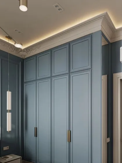 A close-up of the blue paneled wardrobe, showing the clean lines and classic design. The integrated lighting in the ceiling cove adds a soft glow to the entire room.