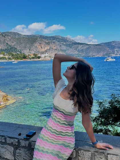 A candid moment by the sea. The off-shoulder design of this knit dress adds a touch of summer romance, perfect for a European holiday.