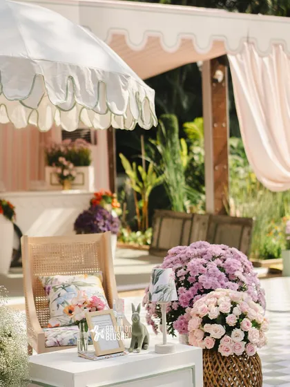 A cozy corner with a rattan chair, floral cushion, and large bouquets of pink and purple flowers.