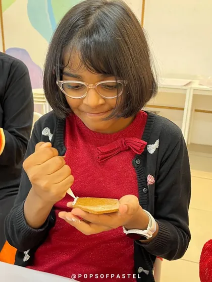 A young girl focuses on carefully placing a piece of gingerbread, learning patience and precision.