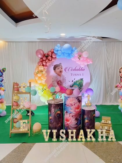 A full stage setup for a Krishna themed first birthday, including character props, themed cake stands, and marquee letters.