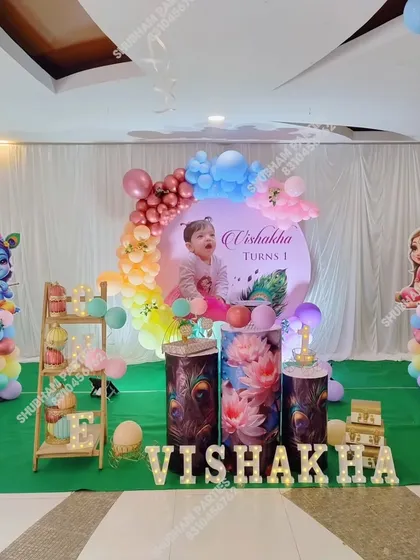 A full stage setup for a Krishna themed first birthday, including character props, themed cake stands, and marquee letters.