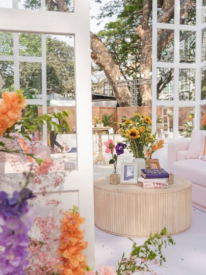 A cozy corner with a pink sofa and a wooden coffee table, decorated with books and sunflowers, offering a quiet space amidst the celebration.