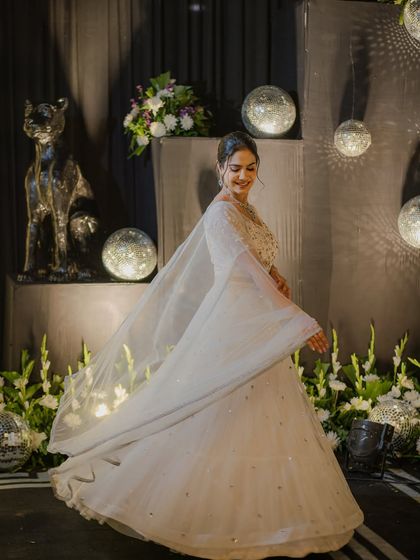 A dreamy, twirling shot in a shimmering white lehenga, surrounded by disco balls and floral decor. Perfect for a glamorous sangeet night.