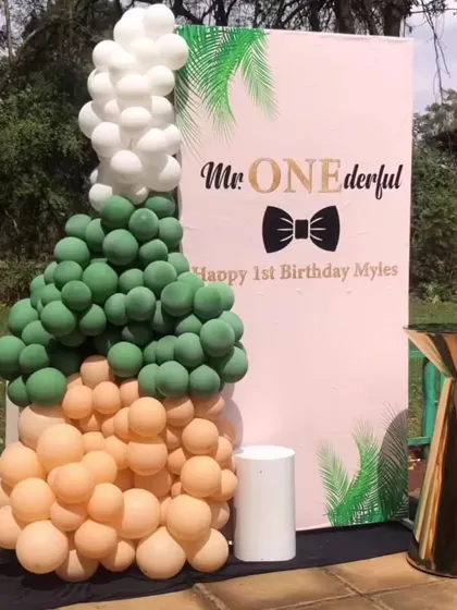 A stylish "Mr. ONEderful" first birthday setup. The decor includes a custom backdrop and a creative balloon sculpture shaped like a champagne bottle popping.