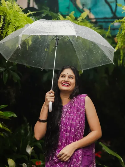A happy moment captured under an umbrella in the rain. Surrounded by lush greenery, the model's upward glance and smile radiate pure joy, making for a lively and uplifting portrait.